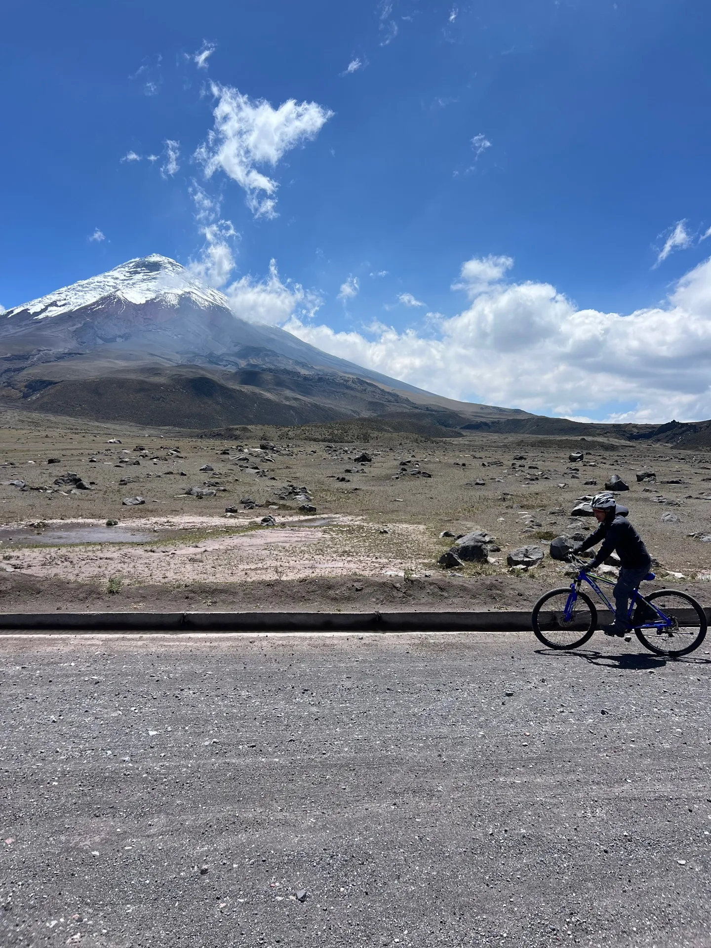 Mountain biker riding a dirt road in Cotopaxi National Park with the snowy volcano behind